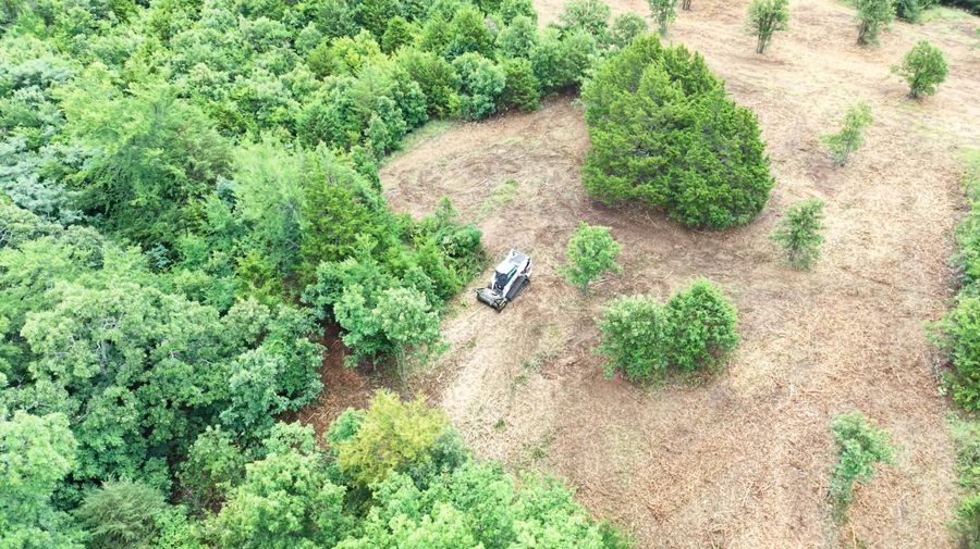 Aerial view of forestry mulching equipment clearing brush along a treeline in Northwest Arkansas